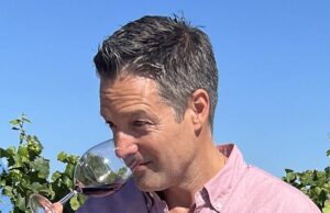 Wine Educator Nick Poletto dipping his nose into a wine glass to smell red wine with a vineyard in the background